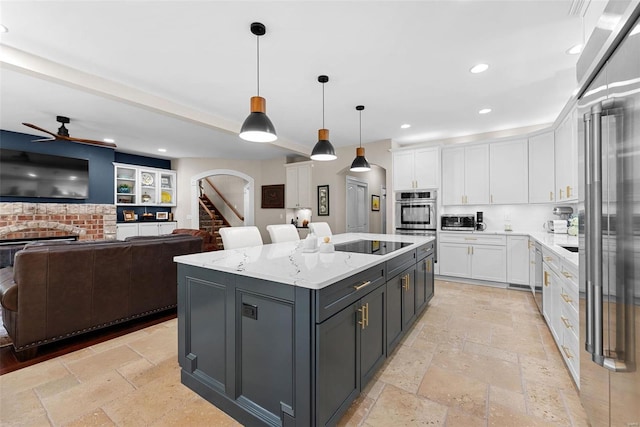 kitchen with appliances with stainless steel finishes, a kitchen island, decorative light fixtures, white cabinets, and light stone counters