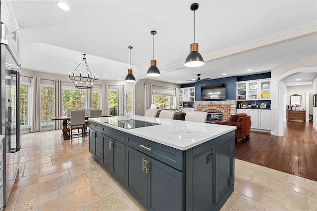 kitchen with light wood-type flooring, a center island, a brick fireplace, white cabinetry, and decorative light fixtures