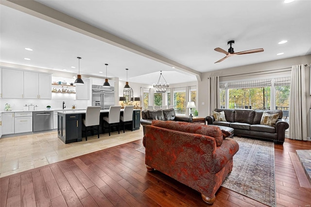 living room with beam ceiling, wood-type flooring, sink, and ceiling fan with notable chandelier