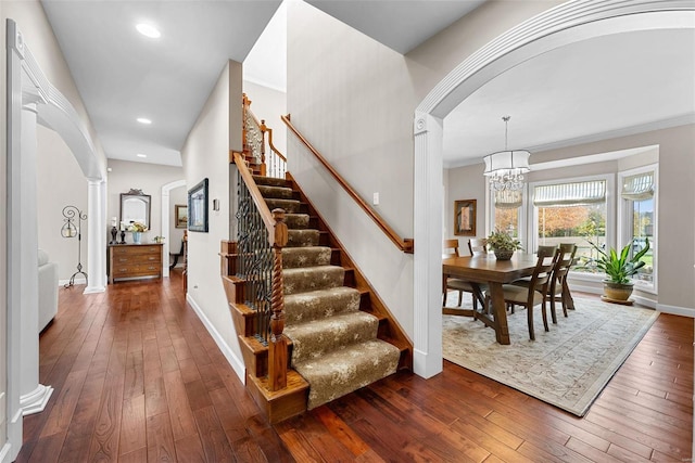 staircase with ornamental molding, an inviting chandelier, hardwood / wood-style floors, and ornate columns