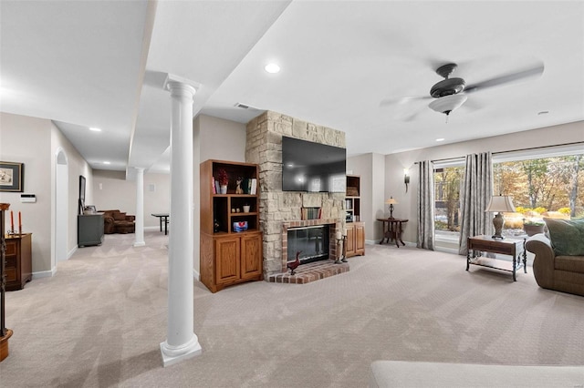 carpeted living room with a fireplace, ornate columns, and ceiling fan