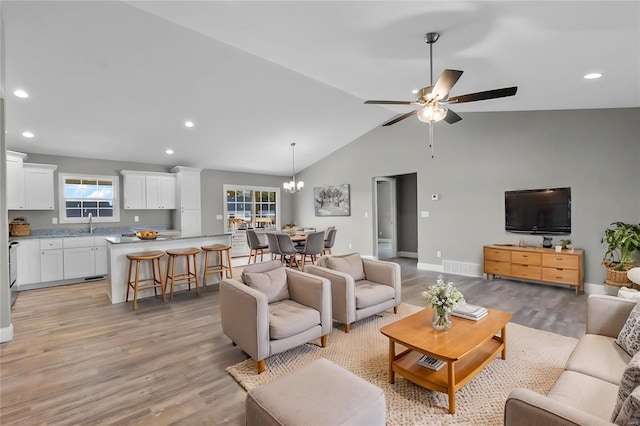 living room featuring sink, high vaulted ceiling, ceiling fan with notable chandelier, and light wood-type flooring