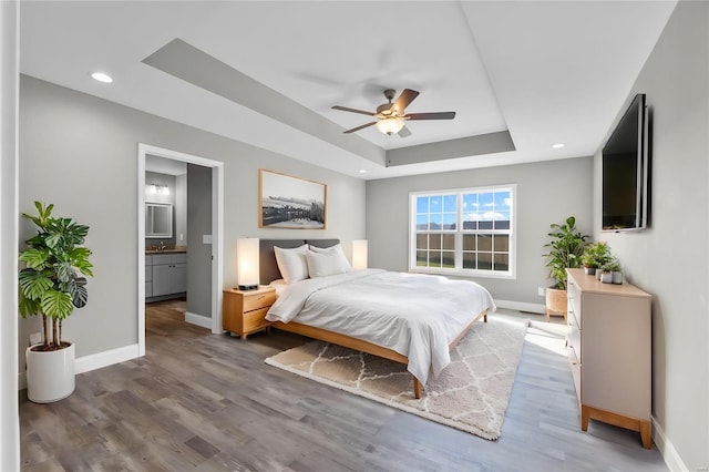 bedroom with a raised ceiling, sink, ensuite bath, ceiling fan, and wood-type flooring