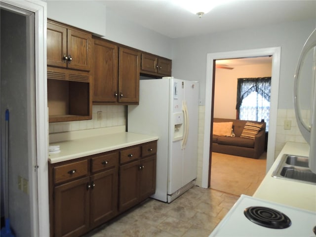 kitchen with white refrigerator with ice dispenser, dark brown cabinetry, tasteful backsplash, and sink