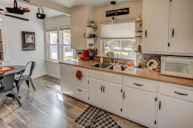 kitchen featuring white cabinetry, light hardwood / wood-style floors, sink, and hanging light fixtures