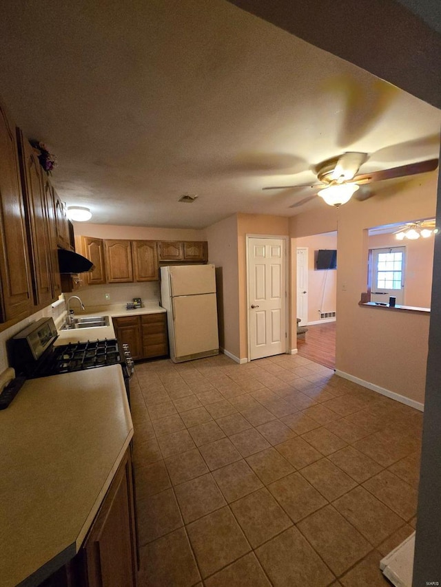 kitchen with light tile patterned flooring, stove, ventilation hood, sink, and white fridge