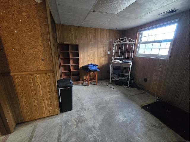 empty room featuring wooden walls, a drop ceiling, and concrete flooring