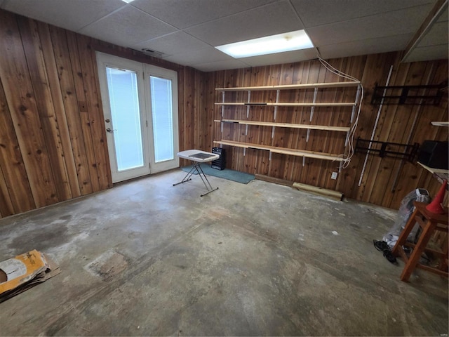 interior space featuring a drop ceiling, concrete flooring, and wooden walls