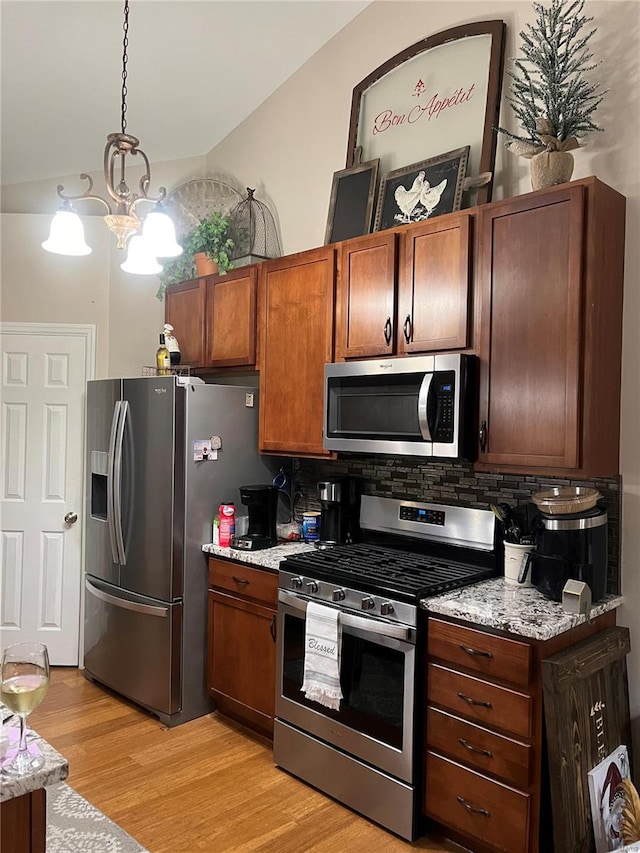 kitchen featuring backsplash, appliances with stainless steel finishes, light stone countertops, light hardwood / wood-style floors, and decorative light fixtures