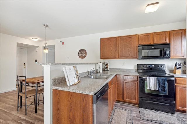 kitchen featuring kitchen peninsula, hanging light fixtures, black appliances, light hardwood / wood-style floors, and sink