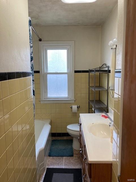 bathroom featuring a tub, tile patterned floors, toilet, vanity, and tile walls