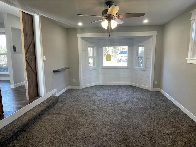 spare room with ceiling fan, dark carpet, and a barn door