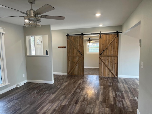 empty room featuring a barn door, ceiling fan, and dark wood-type flooring