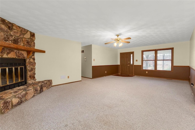 unfurnished living room featuring ceiling fan, a stone fireplace, carpet floors, and a textured ceiling