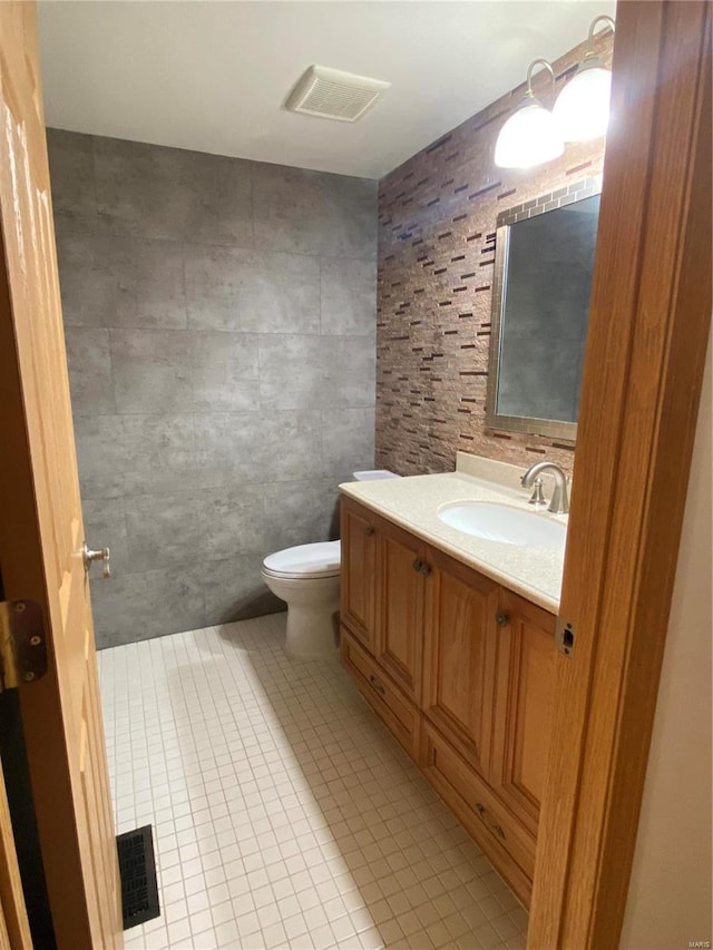 bathroom featuring vanity, toilet, tile walls, and tile patterned flooring