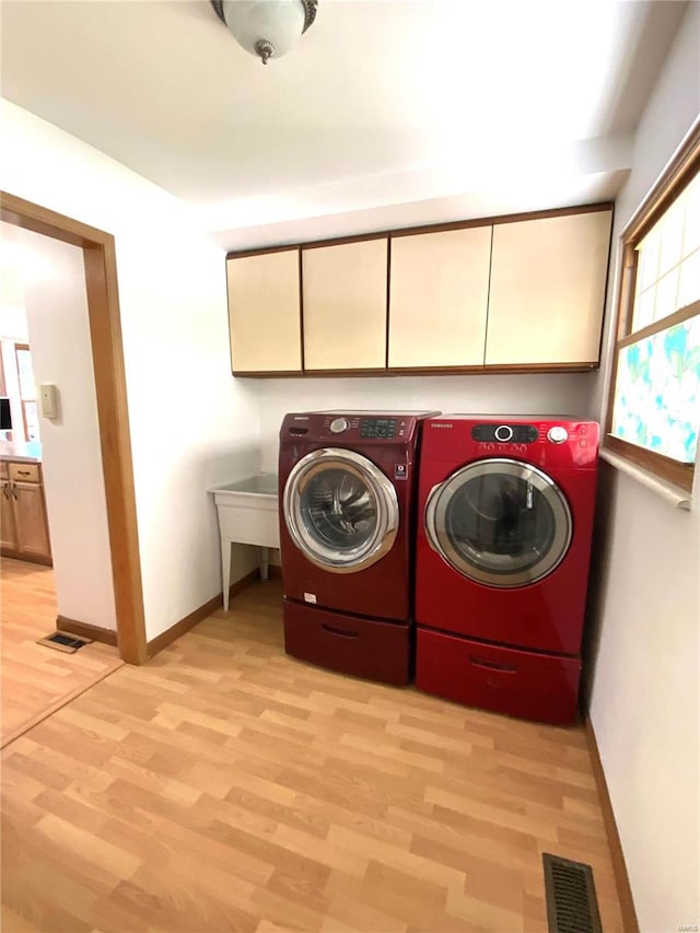 laundry area featuring light hardwood / wood-style flooring, washing machine and dryer, and cabinets