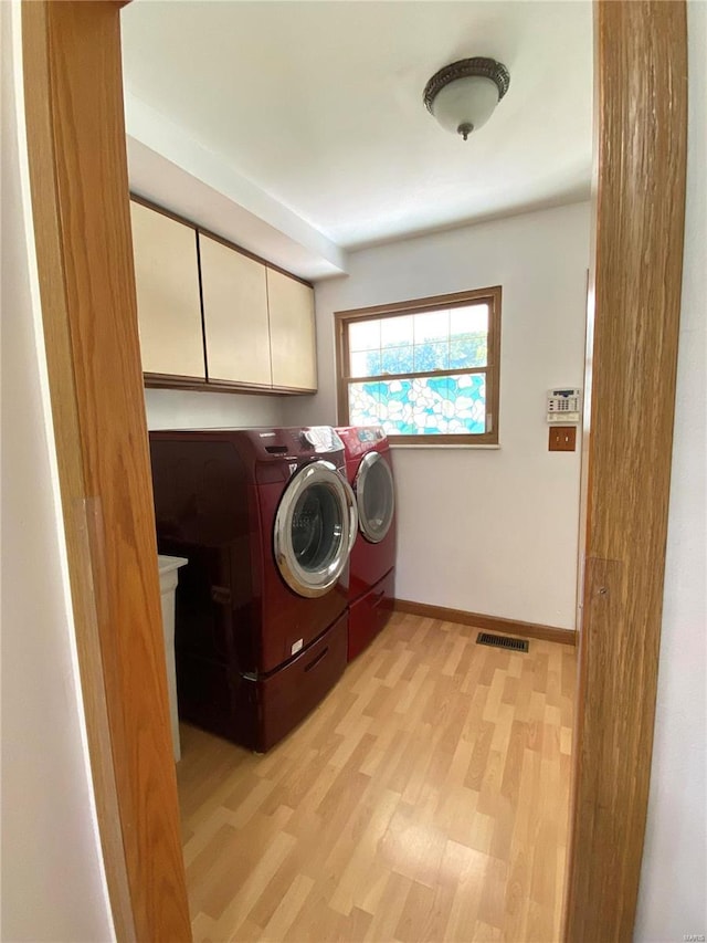 washroom featuring washer and dryer, light hardwood / wood-style floors, and cabinets