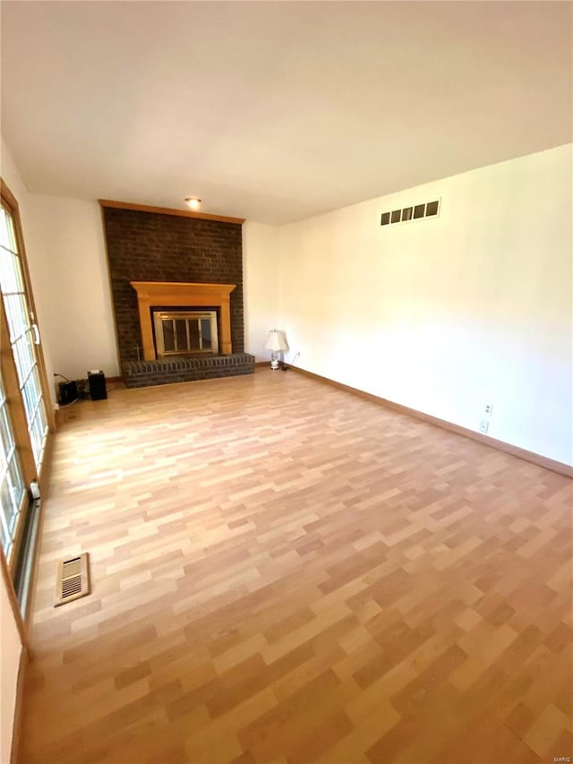 unfurnished living room with wood-type flooring and a brick fireplace