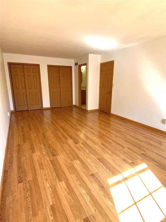 unfurnished bedroom with multiple closets, ensuite bath, and light wood-type flooring