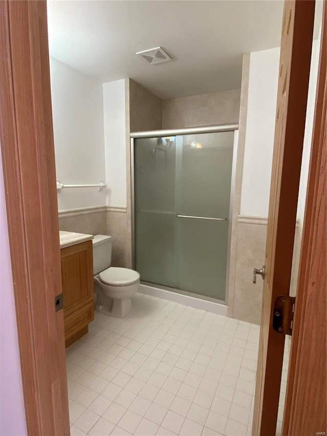 bathroom with a shower with door, tile walls, toilet, vanity, and tile patterned floors