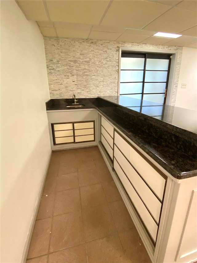 interior space featuring white cabinets, a paneled ceiling, dark stone countertops, sink, and tile patterned flooring