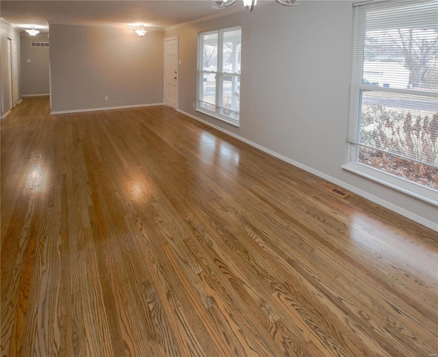 empty room with hardwood / wood-style flooring, ornamental molding, and a chandelier