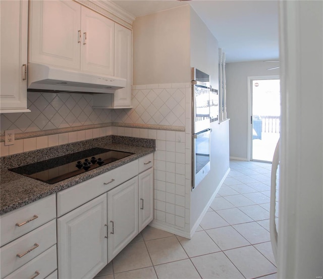 kitchen with multiple ovens, dark stone countertops, black electric cooktop, light tile patterned floors, and white cabinetry