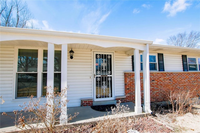 entrance to property with a porch and brick siding