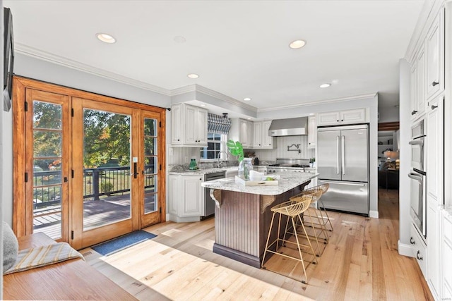 kitchen with a kitchen island, wall chimney range hood, light hardwood / wood-style flooring, white cabinets, and appliances with stainless steel finishes