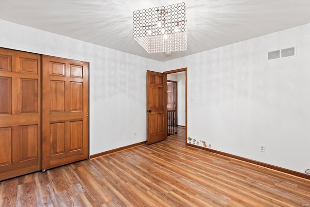 unfurnished bedroom with a closet, a notable chandelier, and light wood-type flooring