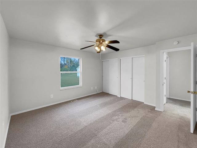 unfurnished bedroom featuring carpet floors, multiple closets, and ceiling fan