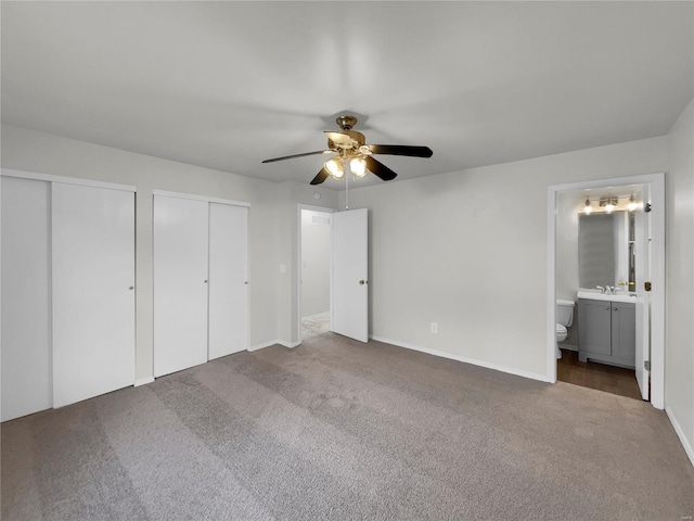 unfurnished bedroom with two closets, carpet, ceiling fan, ensuite bathroom, and sink