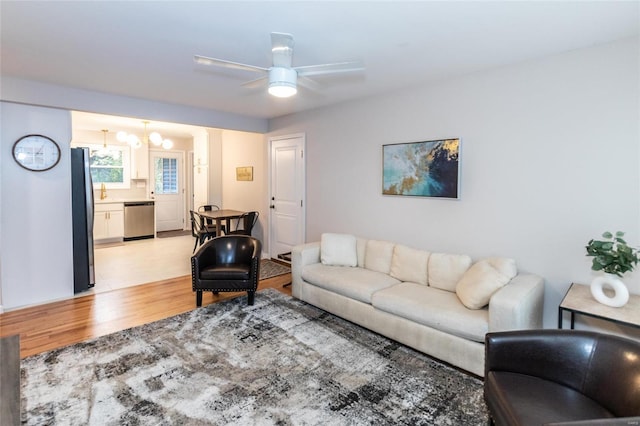 living room featuring ceiling fan with notable chandelier and light wood-type flooring