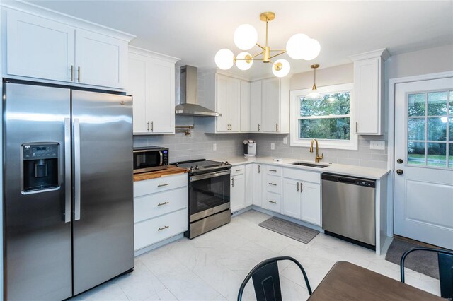 kitchen with wall chimney exhaust hood, appliances with stainless steel finishes, decorative light fixtures, and white cabinets