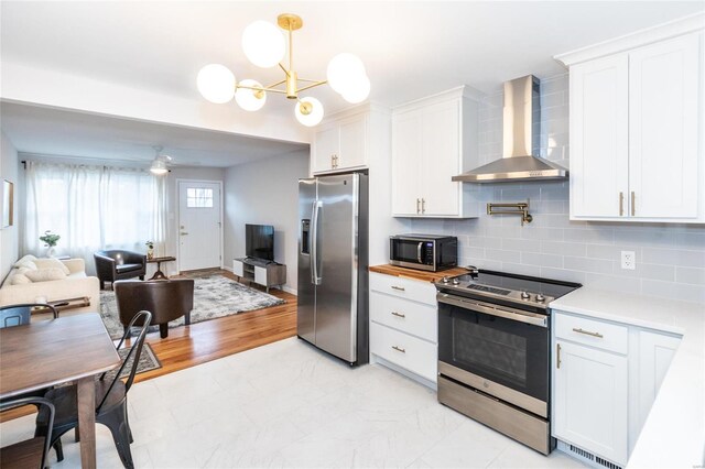 kitchen featuring wall chimney range hood, decorative backsplash, appliances with stainless steel finishes, white cabinetry, and light hardwood / wood-style floors