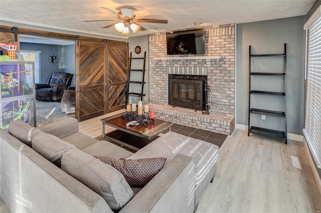 living room with a barn door, wood-type flooring, a fireplace, and ceiling fan