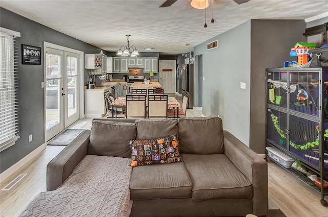 living room featuring light hardwood / wood-style flooring, french doors, a textured ceiling, and ceiling fan with notable chandelier