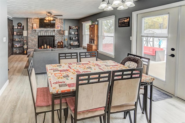 dining space with a textured ceiling, a fireplace, light wood-type flooring, and ceiling fan