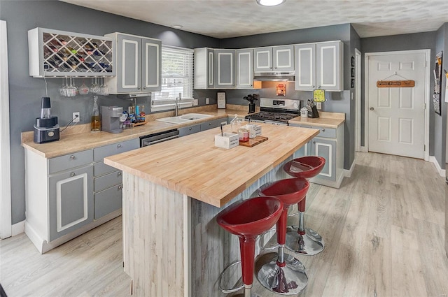 kitchen with a kitchen island, gray cabinetry, a kitchen bar, light wood-type flooring, and appliances with stainless steel finishes