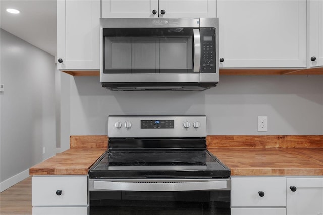 kitchen with stainless steel appliances, white cabinetry, and butcher block counters