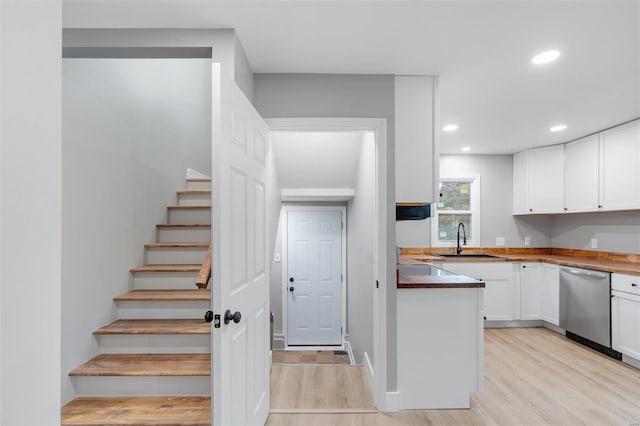 kitchen featuring light wood-type flooring, stainless steel dishwasher, sink, butcher block countertops, and white cabinetry