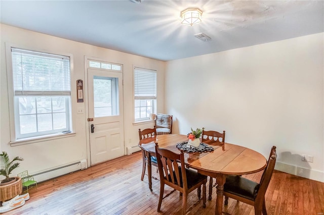 dining area featuring wood-type flooring, a baseboard radiator, and a wealth of natural light