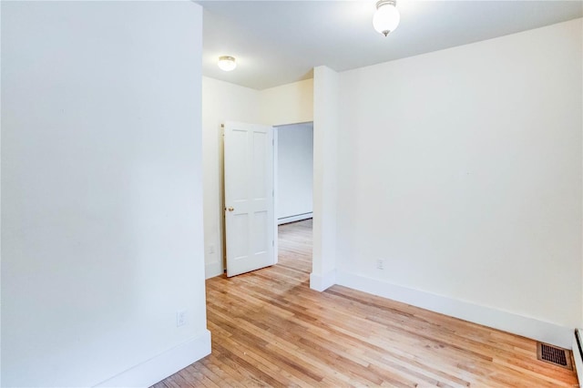 empty room with light hardwood / wood-style floors and a baseboard heating unit