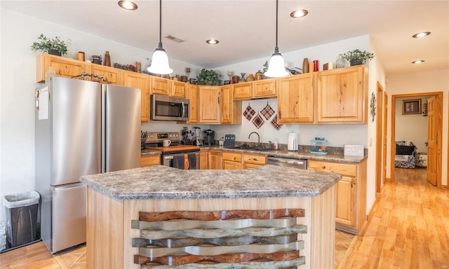 kitchen featuring a center island, stainless steel appliances, decorative light fixtures, light brown cabinetry, and light hardwood / wood-style flooring