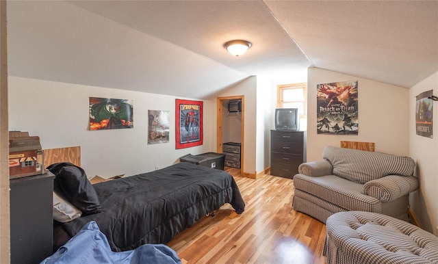 bedroom featuring a textured ceiling, vaulted ceiling, and light hardwood / wood-style flooring