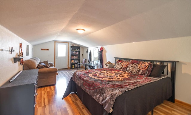 bedroom with vaulted ceiling, light hardwood / wood-style floors, and a textured ceiling