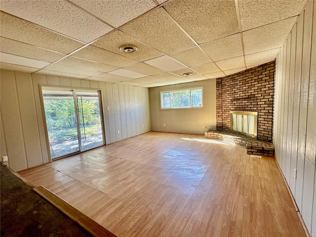 unfurnished living room featuring wooden walls, a fireplace, a paneled ceiling, and light wood-type flooring