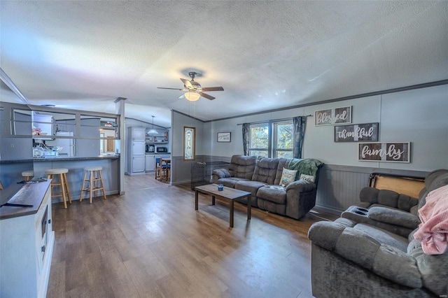 living room with wood walls, wood-type flooring, a textured ceiling, ceiling fan, and vaulted ceiling