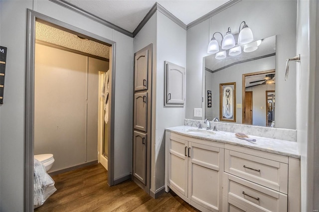 bathroom with toilet, hardwood / wood-style floors, crown molding, vanity, and ceiling fan