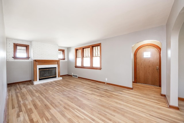 unfurnished living room with a large fireplace, a healthy amount of sunlight, and light wood-type flooring